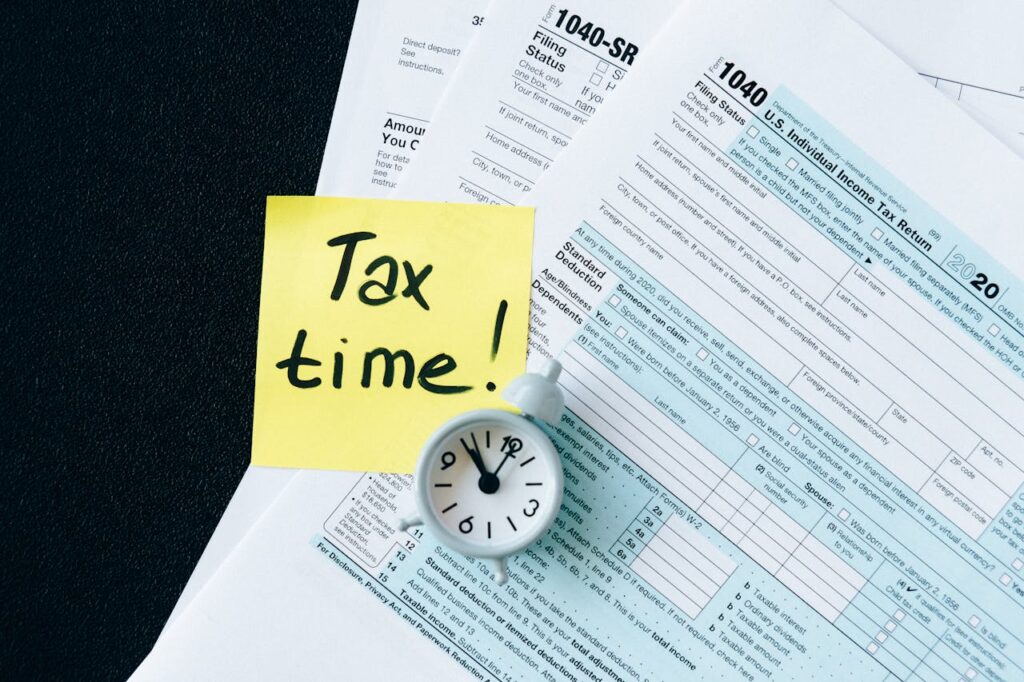 A stack of tax forms with a clock and yellow sticky note saying 'Tax time!' indicating urgency.